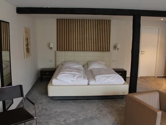 Een tweepersoonsbed in een hotelkamer, omringd door moderne houten elementen en neutrale kleuren.