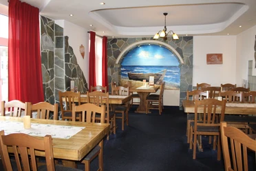 Hotel-Restaurant Platon Rustikales Interieur mit Holztischen, roten Vorhängen und Wandgemälde eines Bootes am Strand.