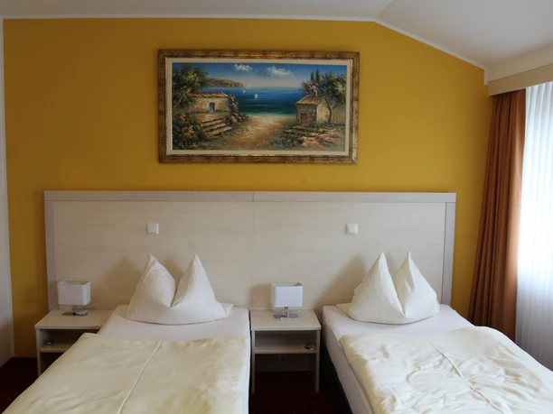 Two single beds with white comforters in a room with a yellow-painted wall and coastal image.