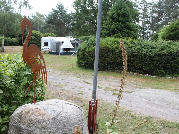 Moorcamp Campingplatz mit einem Wohnwagen im Grünen, rustikale Flamingo-Skulptur und üppige Vegetation.