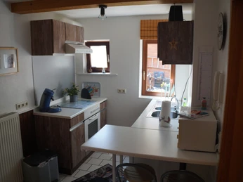 Ferienwohnung Wehrmann Kompakte Küche mit Herd, Kaffeemaschine, Spüle und Holzmöbeln, mit Blick auf ein helles Fenster.Compact kitchen with stove, coffee machine, sink and wooden furniture, overlooking a bright window.Kompakt køkken med komfur, kaffemaskine, vask og træelementer med udsigt til et lyst vindue.Compacte keuken met fornuis, koffiezetapparaat, gootsteen en houten kasten, met uitzicht op een licht raam.