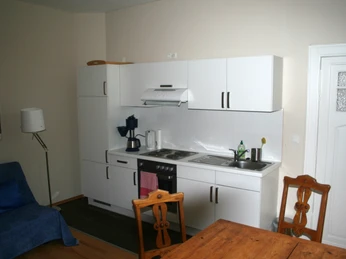 Riederhof 26 Moderne Küchenzeile mit Herd, Dunstabzugshaube, Spüle und weißer Möblierung in wohnlichem Ambiente.