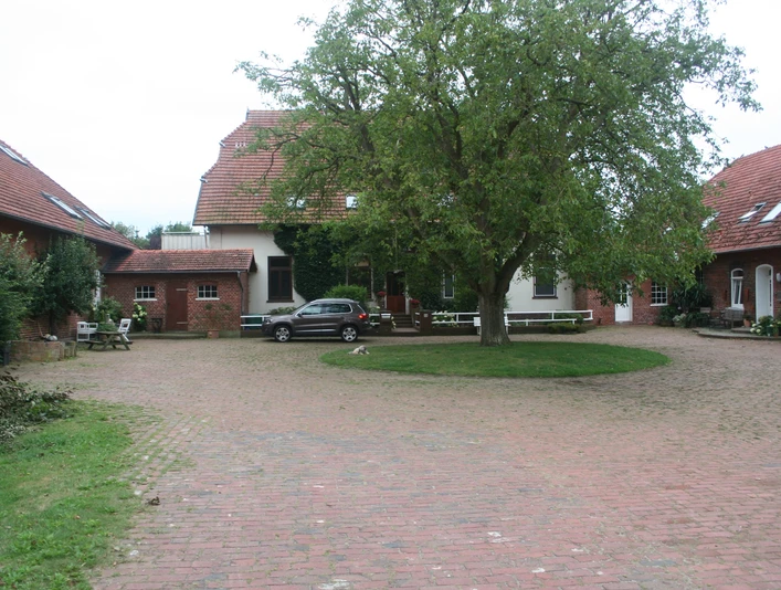 Riederhof 26 Hofgebäude umschließen einen gepflasterten Innenhof mit Baum und geparktem Auto in ländlicher Umgebung.