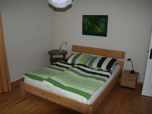 Bedroom with double bed, striped bed linen, bedside table, lamp and artwork on the wall.