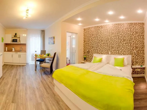 Weyher Aparthotel Ein modernes Hotelzimmer mit Doppelbett, hellen Möbeln und einer kleinen Küchenzeile im Hintergrund.