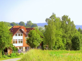 Bildungsstätte Himmighausen - Bildungsstätte im Grünen Rotes Backsteinhaus mit weißen Fensterfronten, umgeben von Wiesen und dichtem Laubwald.
