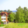 Bildungsstätte Himmighausen - Bildungsstätte im Grünen Rotes Backsteinhaus mit weißen Fensterfronten, umgeben von Wiesen und dichtem Laubwald.