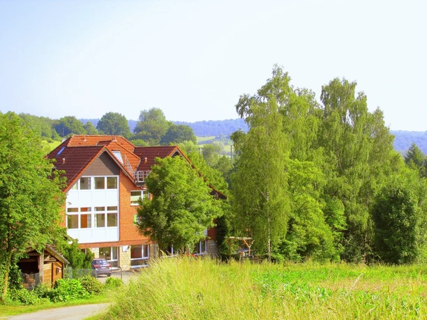Bildungsstätte Himmighausen - Bildungsstätte im Grünen Rotes Backsteinhaus mit weißen Fensterfronten, umgeben von Wiesen und dichtem Laubwald.