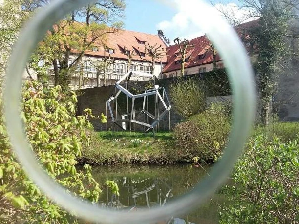 Eine moderne Skulptur spiegelt sich im Wassergraben des historischen Schloss Brake wider.