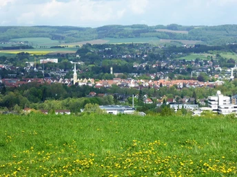 Aussicht vom Biesterberg Blick über eine grüne Wiese hinweg auf eine Stadtlandschaft mit Kirche im Vordergrund und Hügeln im Hintergrund.
