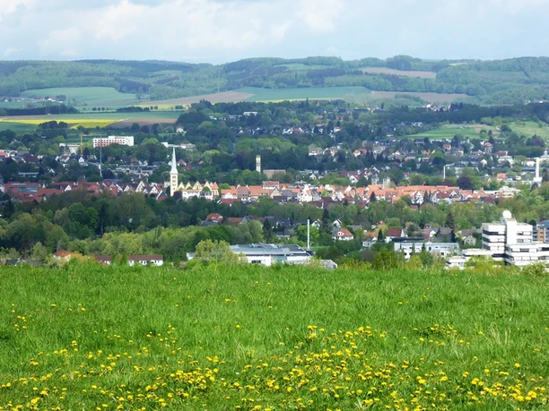 Aussicht vom Biesterberg Blick über eine grüne Wiese hinweg auf eine Stadtlandschaft mit Kirche im Vordergrund und Hügeln im Hintergrund.