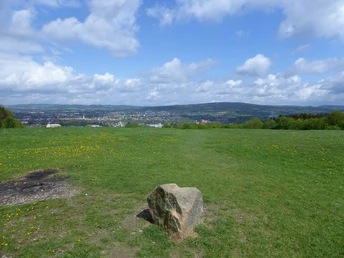 Aussicht vom Biesterberg Von einem sanften Hügel bietet sich ein weiter Blick über eine grüne Wiese auf eine Stadt in der Ferne.