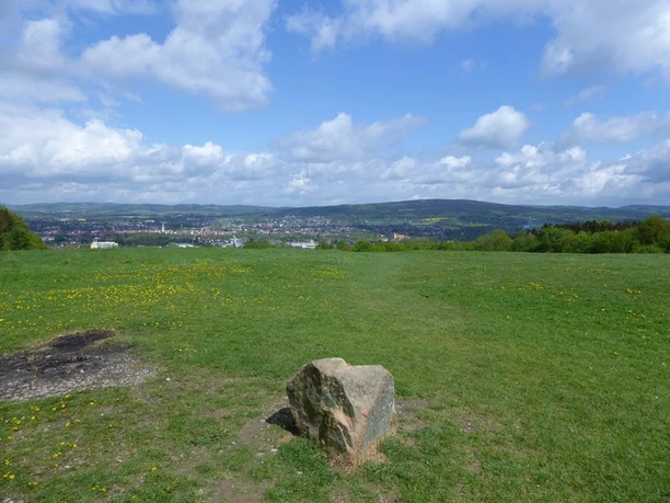 Aussicht vom Biesterberg Von einem sanften Hügel bietet sich ein weiter Blick über eine grüne Wiese auf eine Stadt in der Ferne.