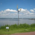 Metallskulptur von Jörg Wiele am Steinhuder Meer, mit Segelbooten und Wolkenhimmel im Hintergrund.