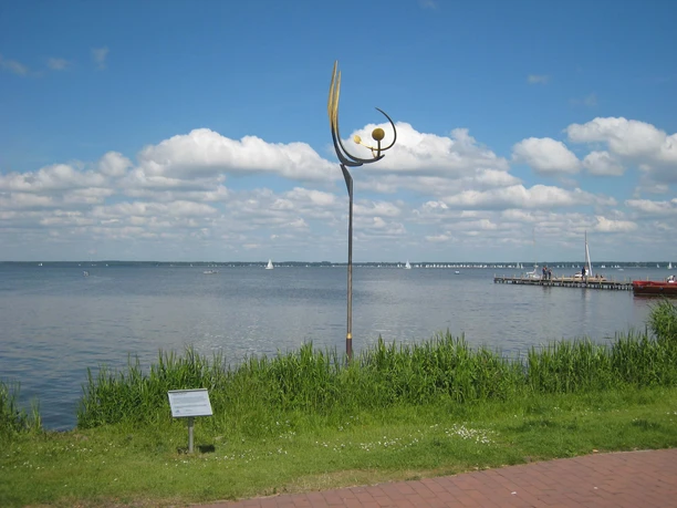Metal sculpture by Jörg Wiele on the Steinhuder Meer, with sailing boats and a cloudy sky in the background.