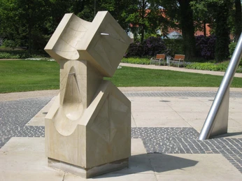 "Sonnenuhr" von Klaus Wolf Simon Sonnenuhr-Skulptur aus hellem Stein im Park, umgeben von Grünflächen und Bäumen, zeitlos designt.Sundial sculpture made of light-colored stone in the park, surrounded by green spaces and trees, timeless design.Solurskulptur af lys sten i parken, omgivet af grønne områder og træer, tidløst design.Zonnewijzer sculptuur van lichtgekleurde steen in het park, omgeven door groen en bomen, tijdloos ontwerp.