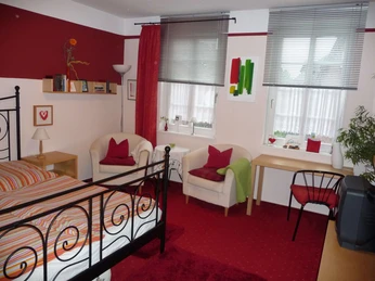 fewo-kuenstlerhauspotthast-wohnung1-schlafzimmer Metallgitterbett mit zwei Cocktailsesseln und Tisch am Fenster