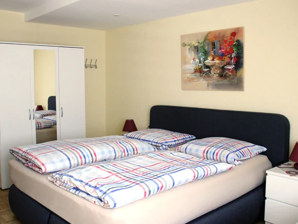 pension-zurweser-doppelzimmer Doppelzimmer mit großem Bett, Nachtkästchen, Kleiderschrank und farbenfrohem Wandbild.