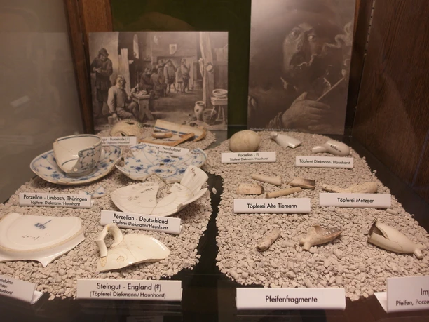 Töpfereimuseum Hagen aTW Ausgrabungsstücke Porzellanscherben und Pfeifenfragmente in einer Vitrine auf Kieselsteinen ausgestellt.