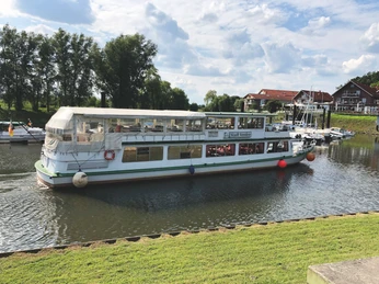 Flusskreuzfahrtschiff MS Stadt Verden an einem sonnigen Tag im Hafen von Achim mit grünem Ufer.
