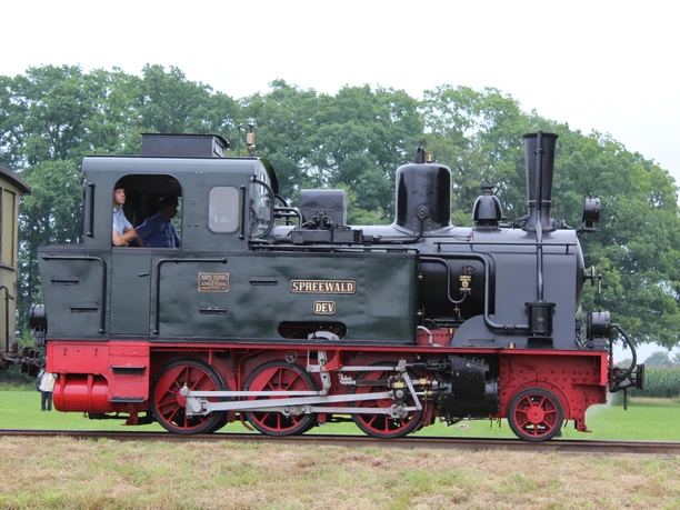 Historic steam locomotive named "Spreewald" on a green meadow with trees in the background, photographed from the side.