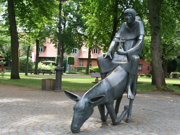 Skulptur Esel und Mönch - Gründungslegende Stiftskirche Bronzeskulptur in einem Park, zeigt einen Mönch auf einem Esel, inspiriert von der Gründungslegende.