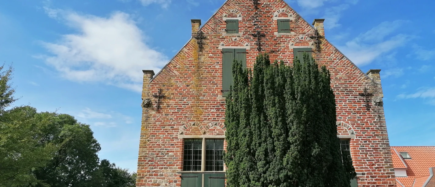 Steinhaus Greetsiel Backsteinbau mit grünen Fensterläden und markanter Giebelfront, teils verdeckt durch hohen Baum.
