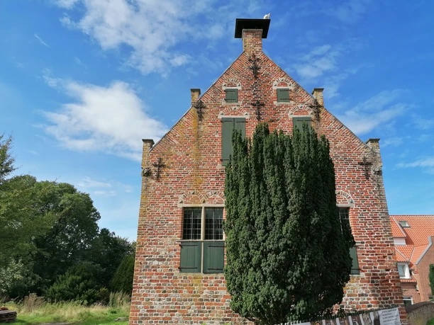 Steinhaus Greetsiel Backsteinbau mit grünen Fensterläden und markanter Giebelfront, teils verdeckt durch hohen Baum.