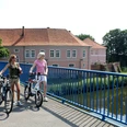 Zwei Frauen auf Fahrrädern überqueren eine Brücke vor dem historischen Grafenschloss in Hoya.