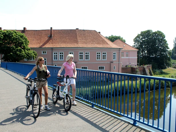 Two women on bicycles cross a bridge in front of the historic Count's Castle in Hoya.
