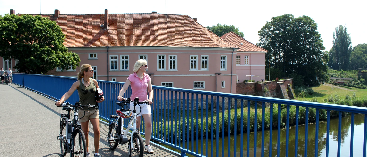 Radfahrer vor dem Grafenschloss in Hoya Zwei Frauen auf Fahrrädern überqueren eine Brücke vor dem historischen Grafenschloss in Hoya.