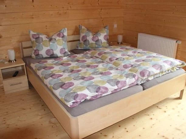 Ferienhaus Breibach Ein gemütliches Schlafzimmer aus hellem Holz mit Doppelbett und farbenfroher Bettwäsche in Pastelltönen.