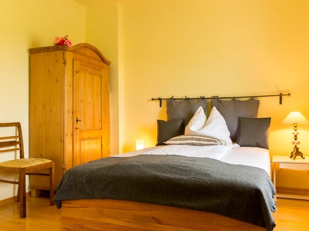 Mediendatei Gemütliches Schlafzimmer mit Holzmöbeln: Doppelbett, Kleiderschrank, Nachttischlampe und Stuhl.