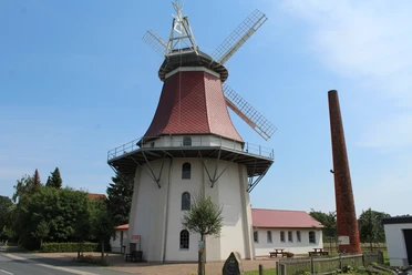 Historic windmill in Emtinghausen, with red roof and wings, surrounded by trees and buildings.