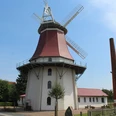 Historische Windmühle in Emtinghausen, mit rotem Dach und Flügeln, umgeben von Bäumen und Gebäuden.