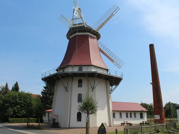 Historic windmill in Emtinghausen, with red roof and wings, surrounded by trees and buildings.