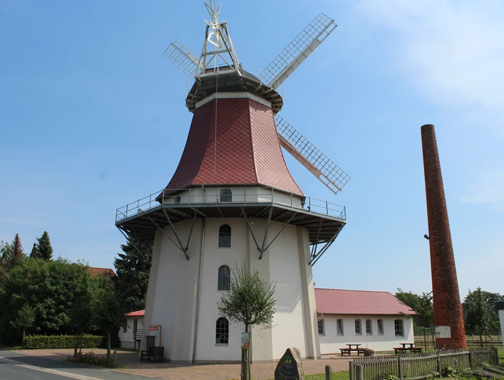 Historische Windmühle in Emtinghausen, mit rotem Dach und Flügeln, umgeben von Bäumen und Gebäuden.