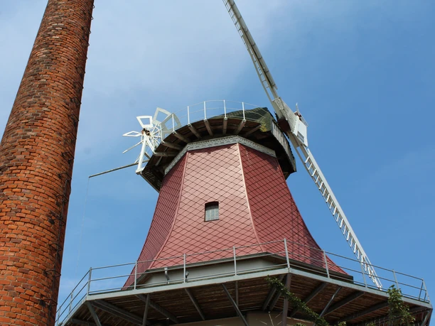 A red Dutch-style gallery windmill with a distinctive brick chimney against a clear blue sky in Emtinghausen.