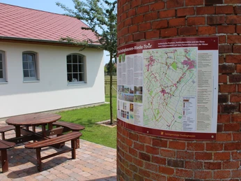A red-brick windmill stands next to a two-sided sign with hiking trail information.