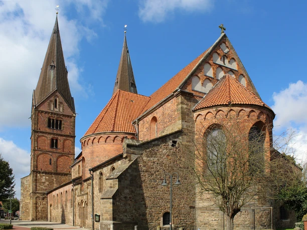 Stiftskirche St. Maternian et St. Nicolai Bücken Romanische Backsteinkirche mit zwei beeindruckenden Türmen und ziegelgedeckten Dächern unter blauem Himmel.