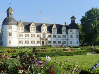 Schloss Neuhaus mit barockem Garten im Vordergrund, Sommerblumen blühen, blauer Himmel im Hintergrund.