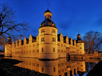 Schloss Neuhaus im Winter, beleuchtet in der Abenddämmerung, spiegelt sich im umgebenden Wassergraben.