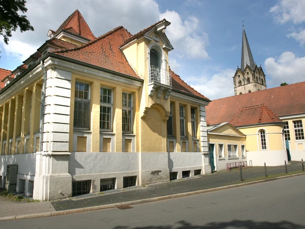 Gelbes Gebäude mit markantem Spitzdach und Turm im Hintergrund, architektonisch ansprechend gestaltet.