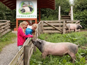 Erlebnis alte Nutzterrassen Zwei Mädchen füttern Schweine auf einem Bauernhof mit grünem Hintergrund und Holzschildern.