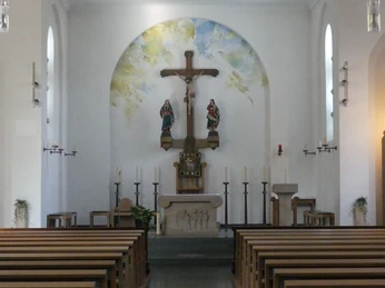 Innenraum von St. Joseph Der Innenraum der St. Joseph Kirche zeigt eine Altaransicht mit Holzkreuz, Heiligenfiguren und Wandgemälde im Hintergrund.