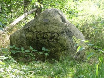 Großer Stein mit eingravierter Jahreszahl 1992, umgeben von dichter Vegetation.