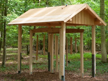 Holzskulptur im Wald mit Dach und hängenden Klängen als Teil der Installation "Baumklänge".