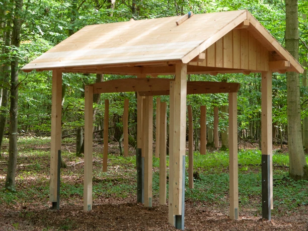 Holzskulptur im Wald mit Dach und hängenden Klängen als Teil der Installation "Baumklänge".