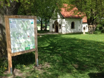 Kapelle "Zur Hilligen Seele" steht hinter einer Wanderwegtafel auf einer grünen Wiese mit Bäumen.