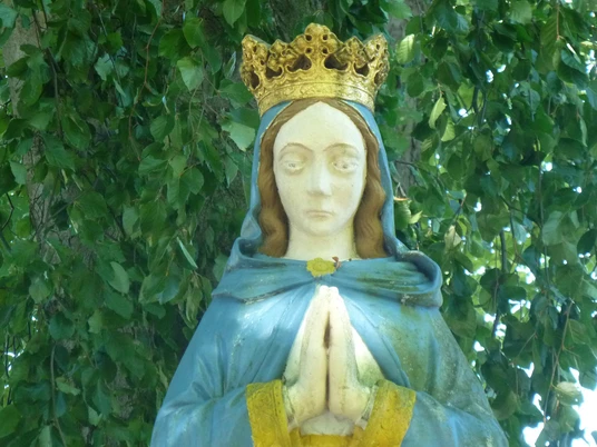 Marienstatue am "Stern", Haxtergrund bei Paderborn Marienstatue mit goldener Krone und betenden Händen, umgeben von grünem Blätterwerk im Haxtergrund.